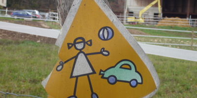 Triangular road sign with damage. Depicting child with ball and car