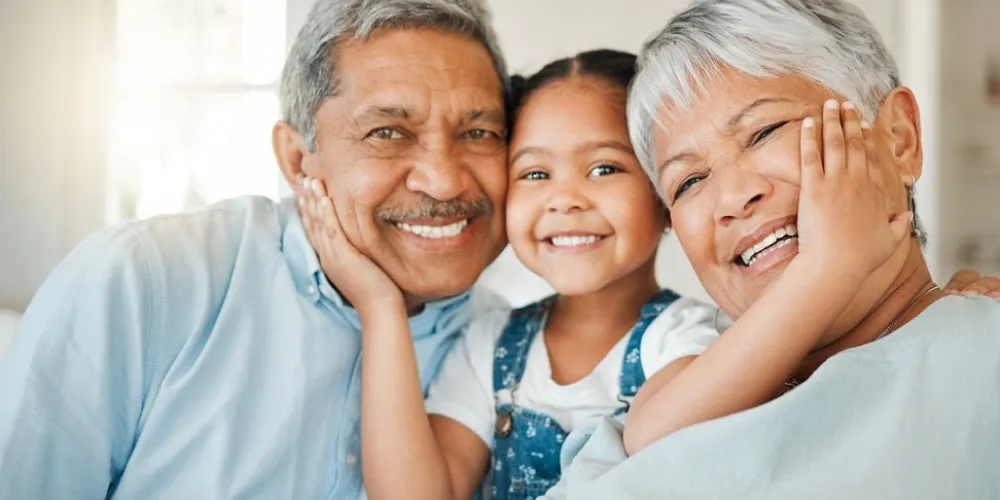 Older woman and man smiling at camera with young girl holding their faces and grinning