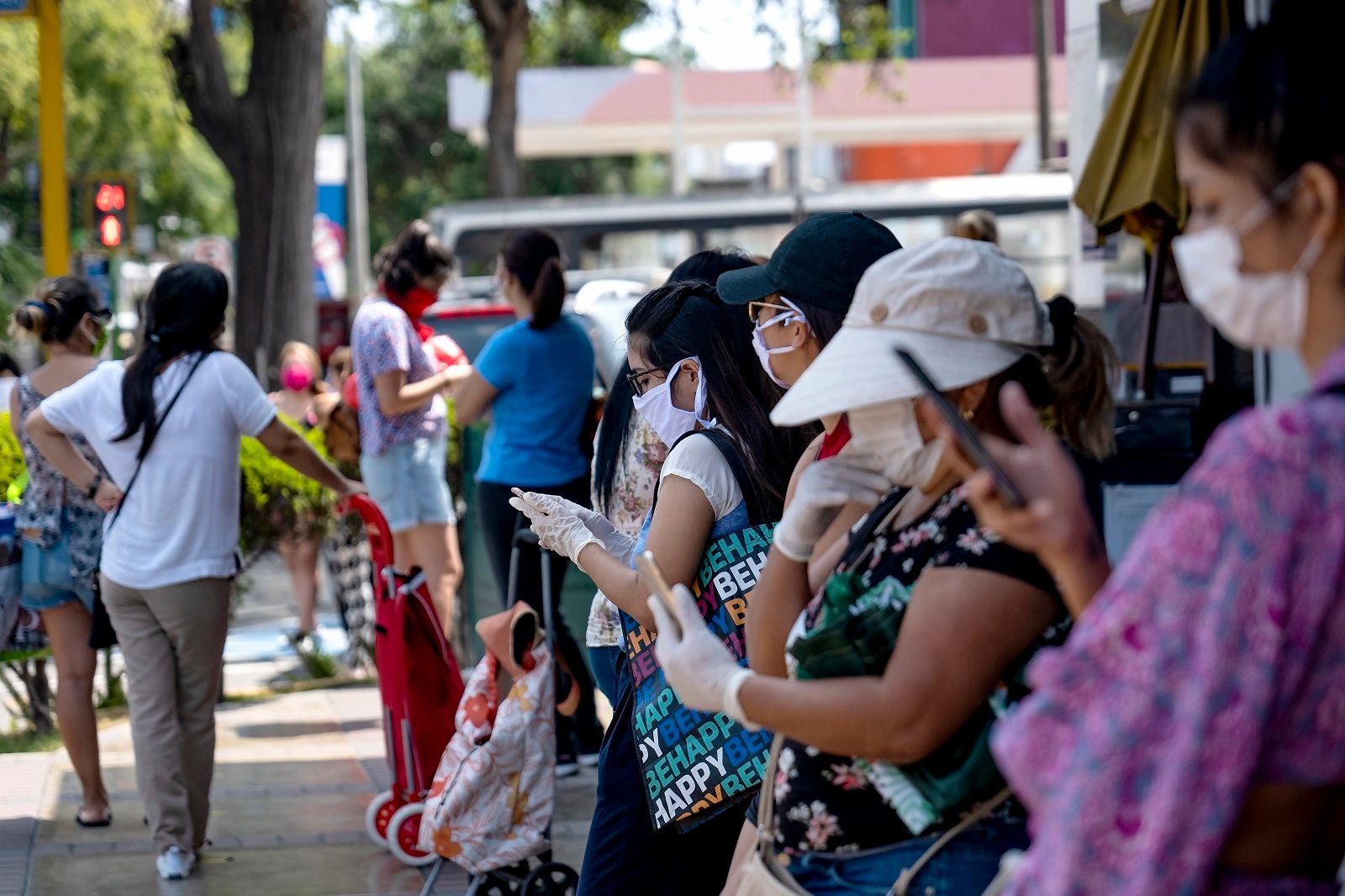 Image of people wearing masks using mobile technology in outdoor location